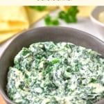 A bowl of spinach dip on wooden board.