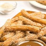 churros and melted chocolate on wooden board.