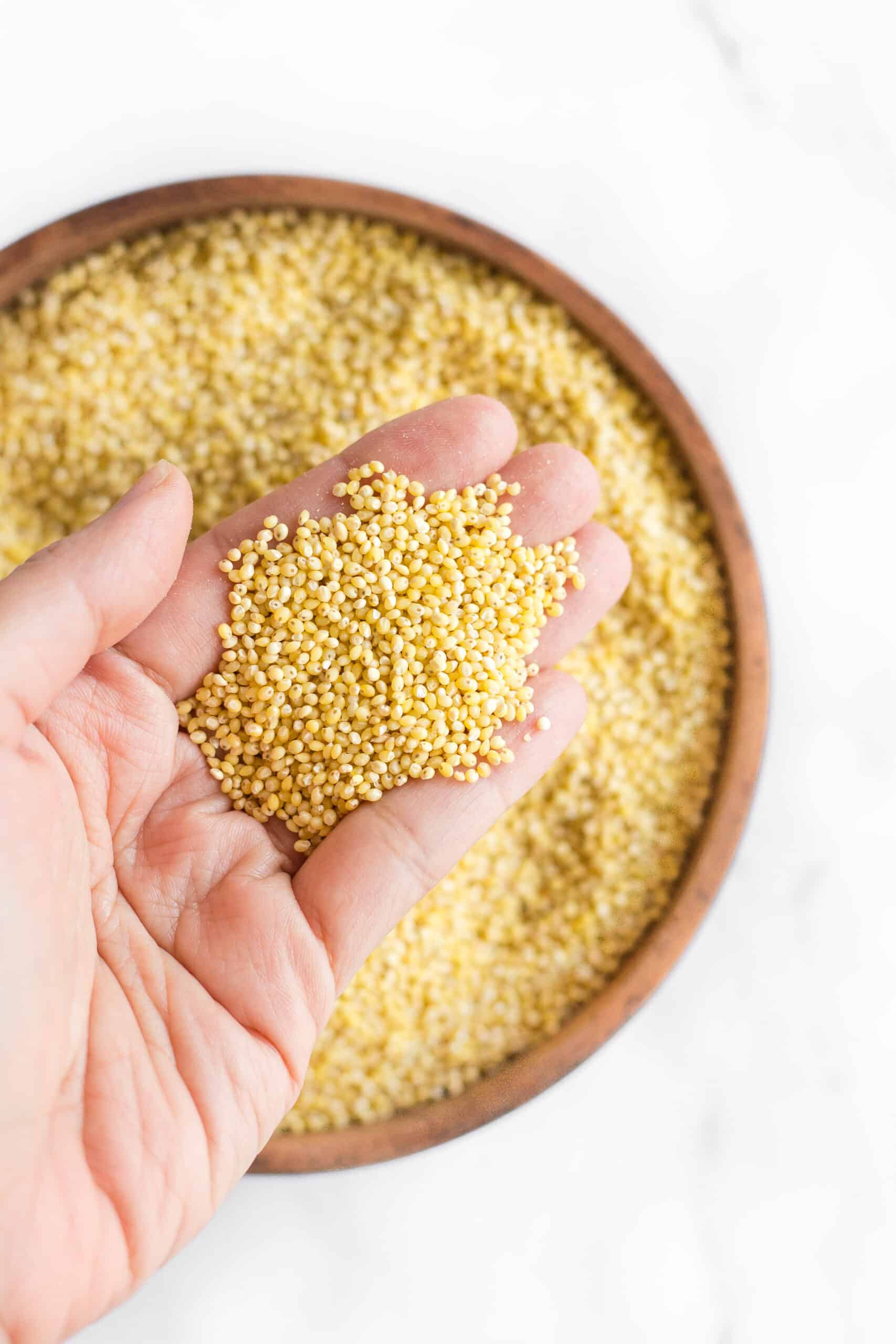 Holding up millet seeds from a wooden bowl.