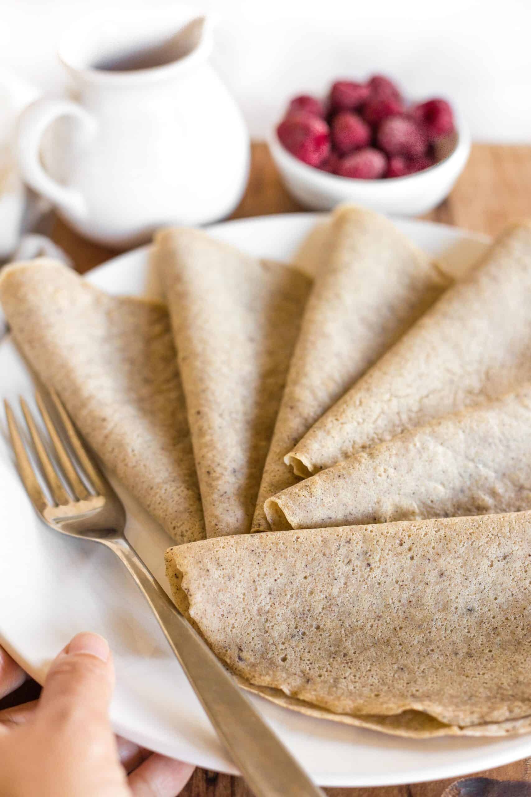 Hand holding a plate with folded millet crepes.