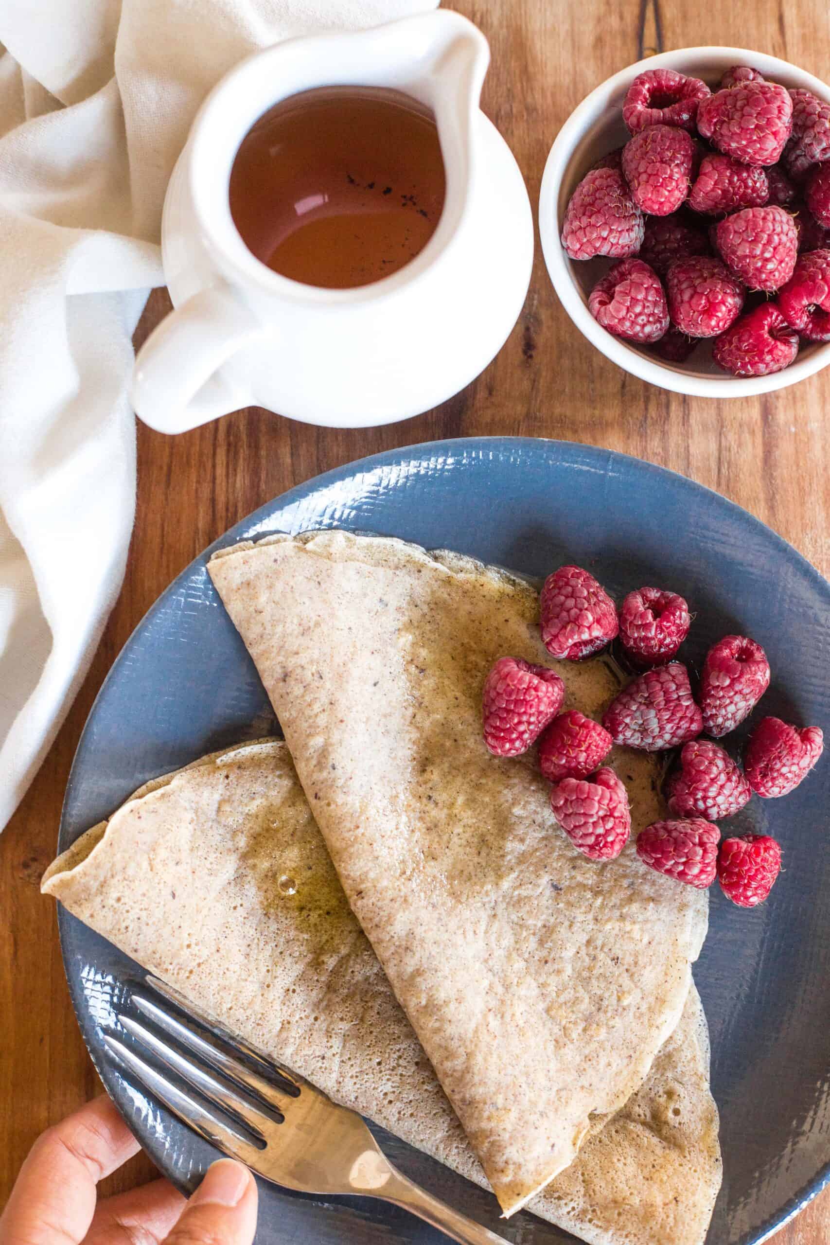 Holding a plate with millet crepes and raspberries.