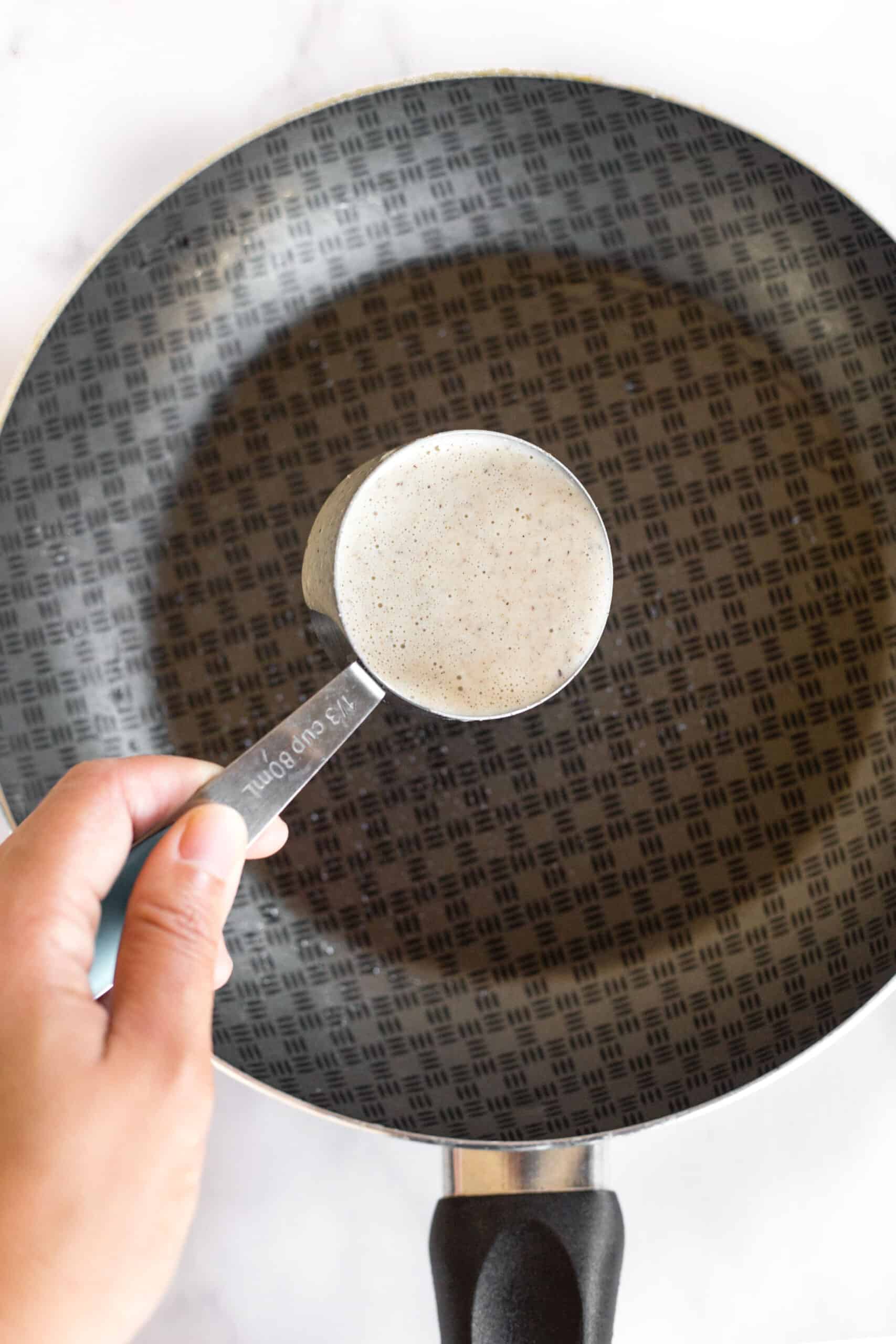 Pouring gluten-free crepe batter into a skillet.