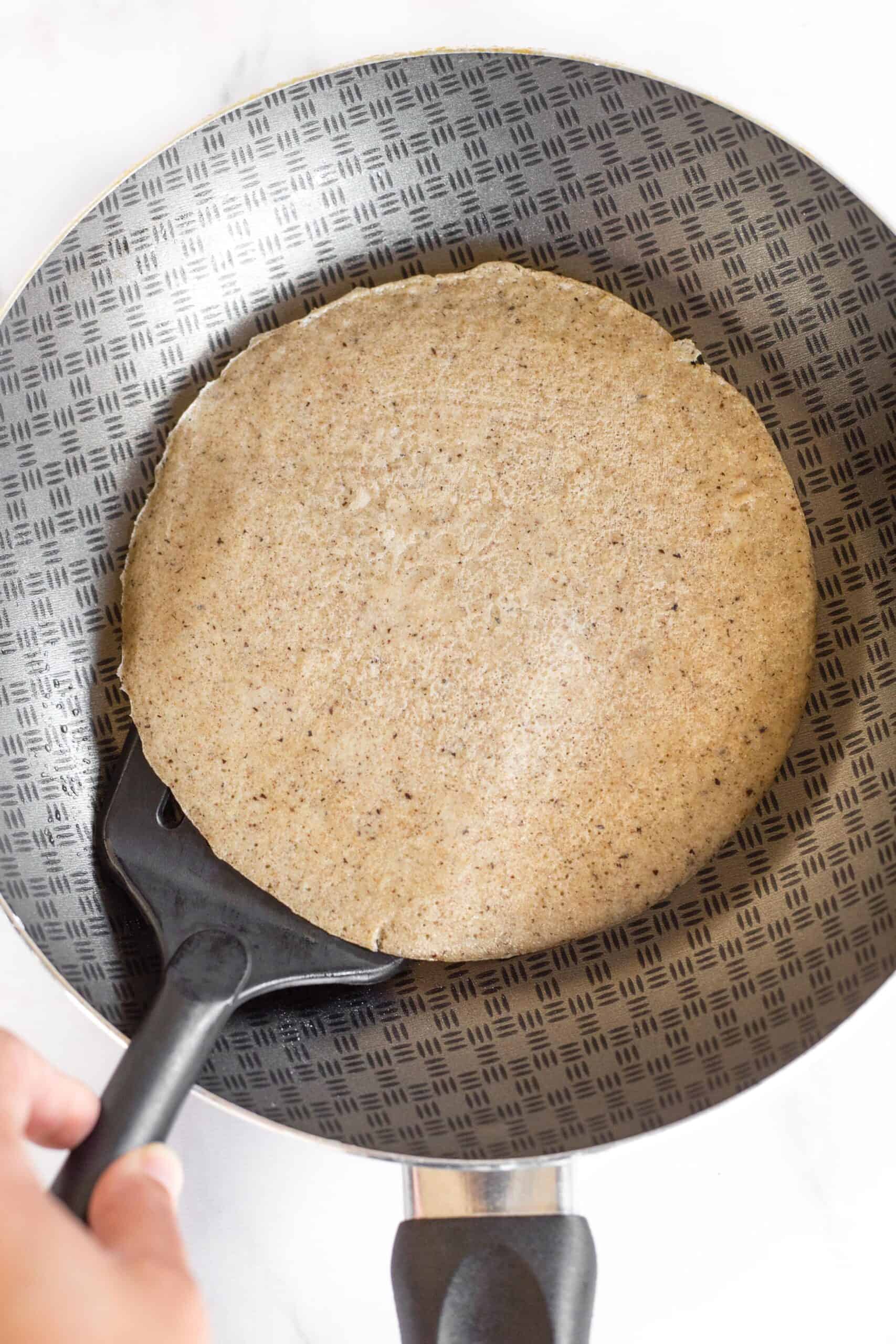 Using a spatula to lift up a cooked buckwheat crepe from a skillet.