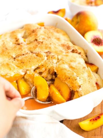 Scooping peach cobbler from casserole dish.