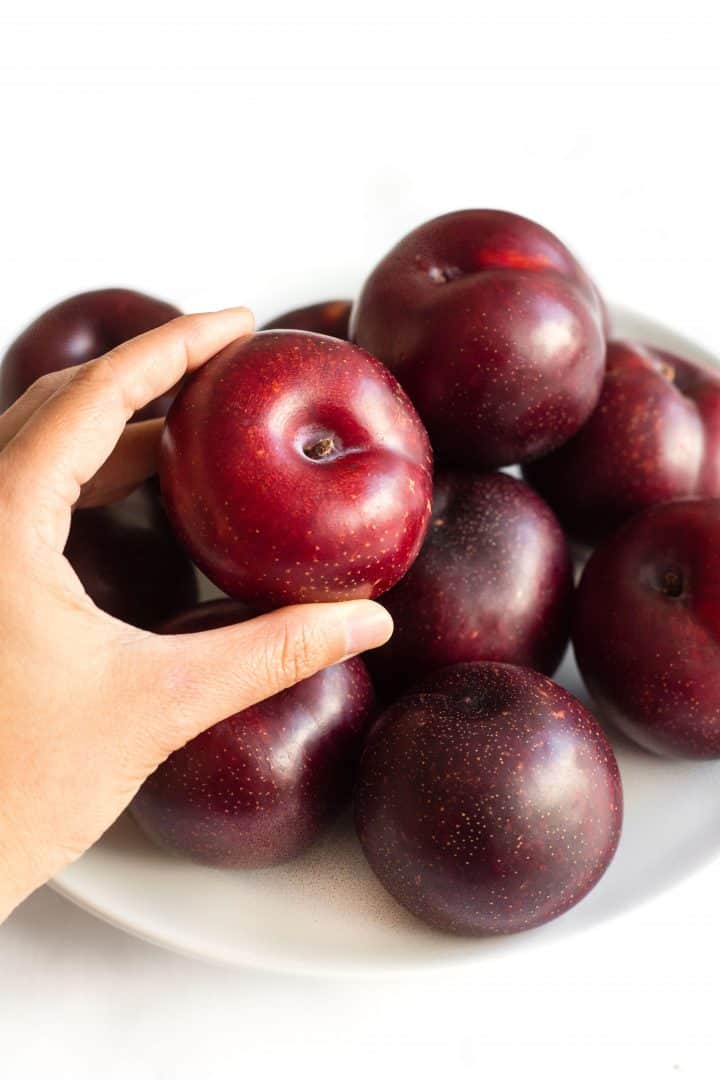 Hand reaching for fresh plums from a plate