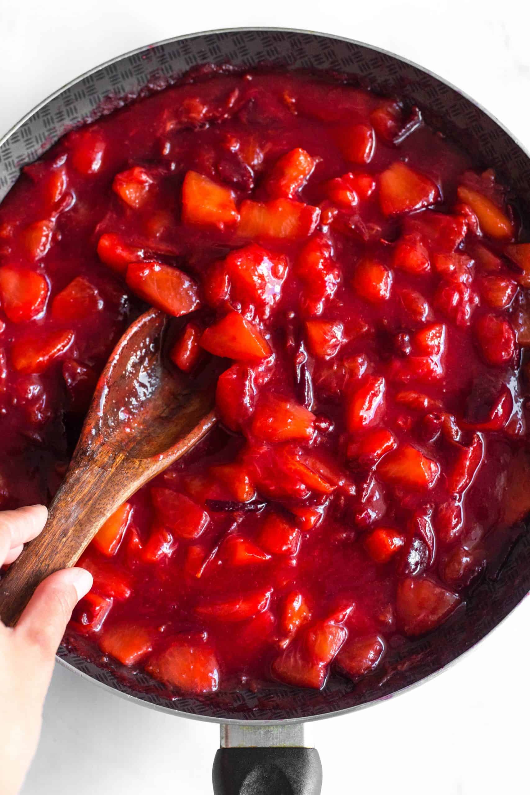 Stirring jam in a skillet with a wooden spoon.
