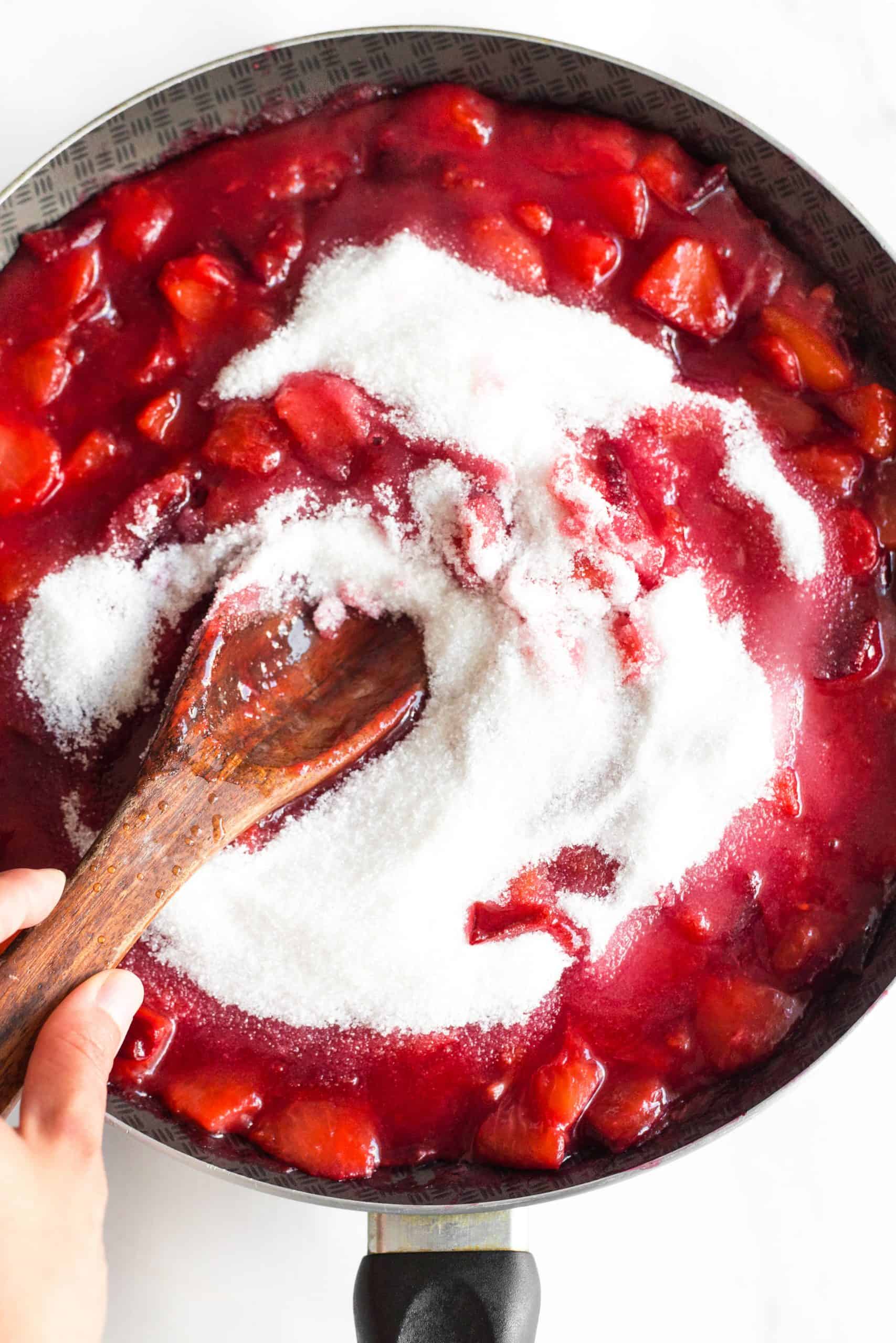 Stirring jam and fruit in a skillet.