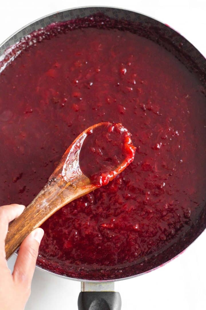 Holding up a spoonful of homemade plum jam from skillet