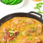 A skillet with chicken thighs in brown gravy