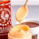 Drizzling sriracha aioli from a spoon into a jar.