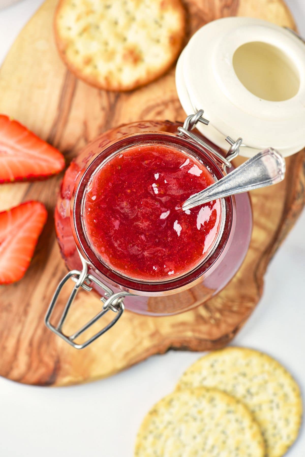 A jar of jam on a wooden board with crackers