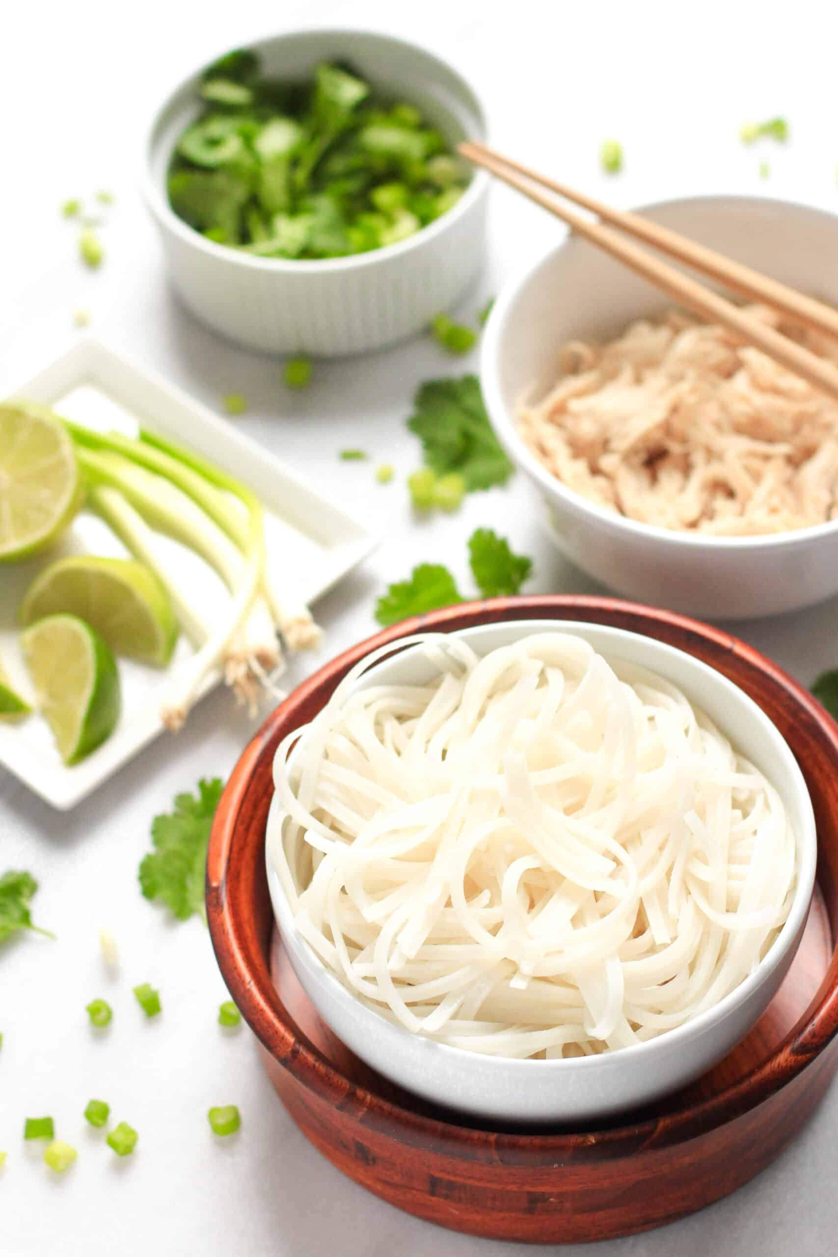 A bowl of rice noodles and shredded chicken in the background.