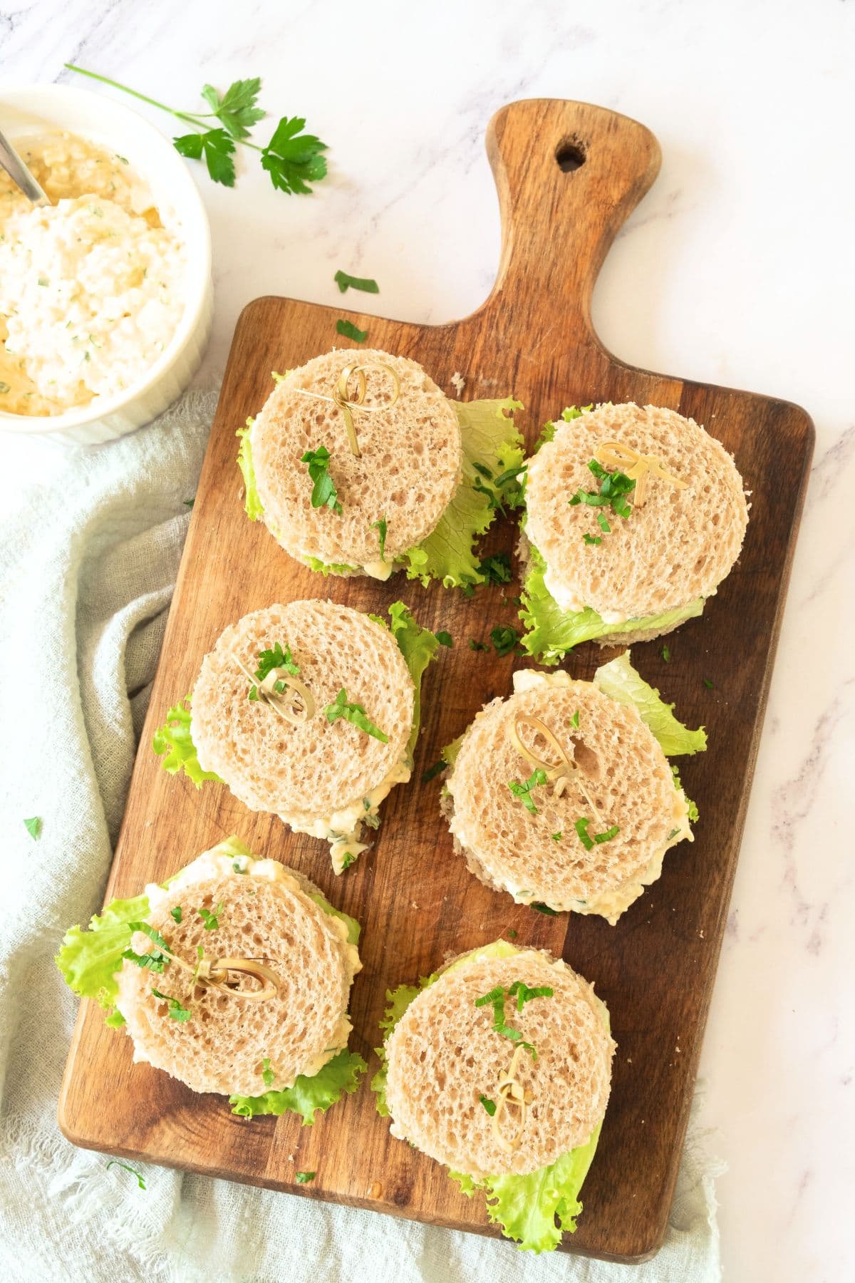 Top down view of mini egg salad sandwiches on wooden board.