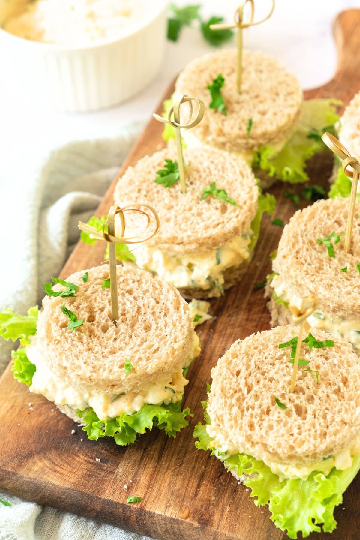 A wooden board with tea party egg salad sandwiches