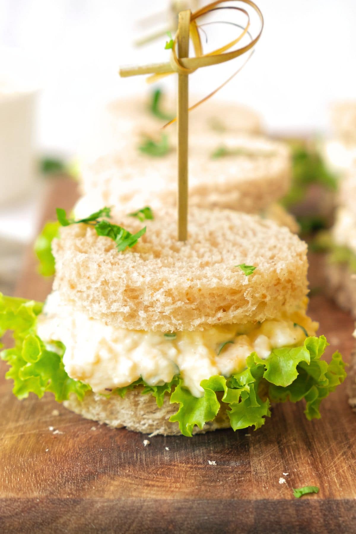 Up close view of egg salad tea party sandwiches on wooden board.