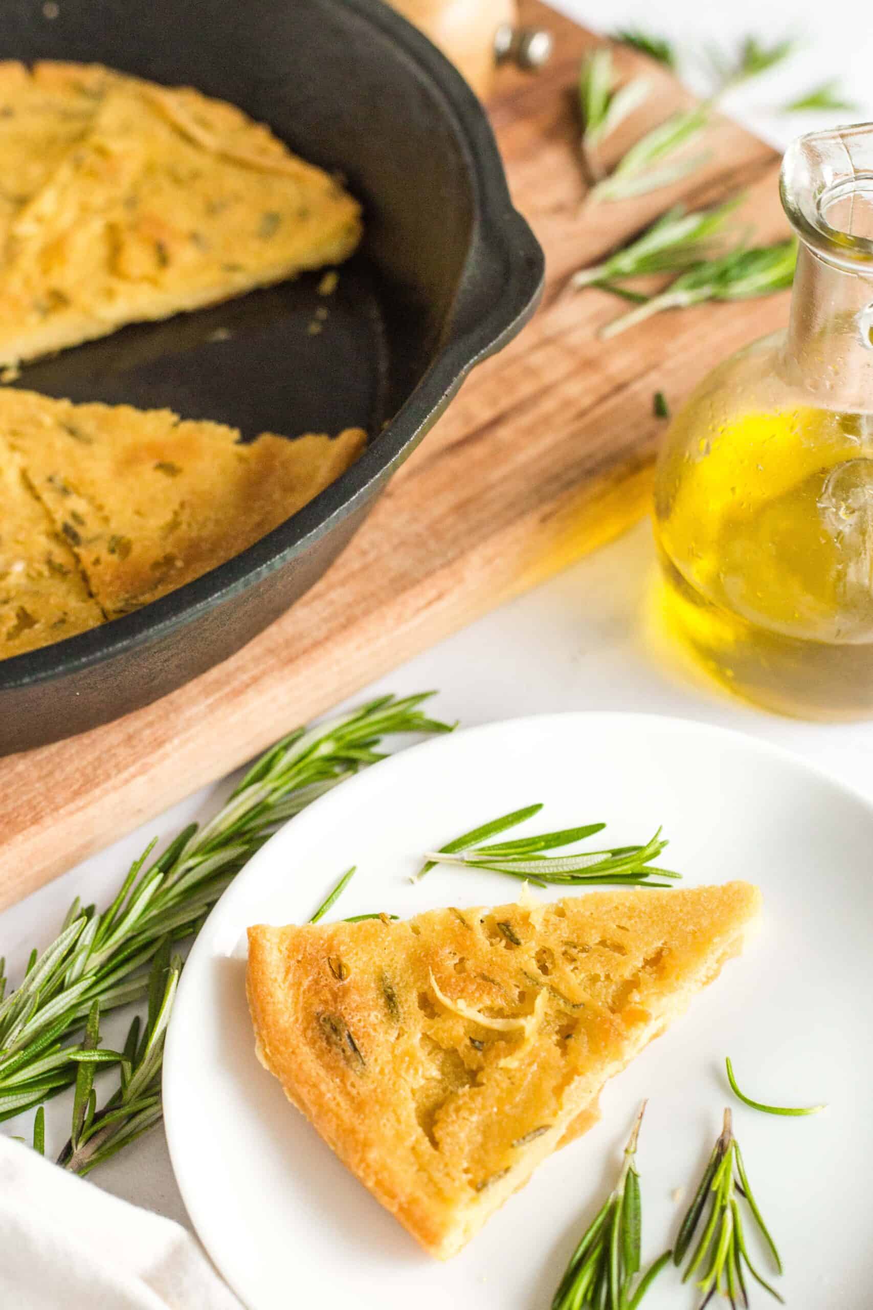 A slice of chickpea flatbread and fresh rosemary leaves on a small plate.