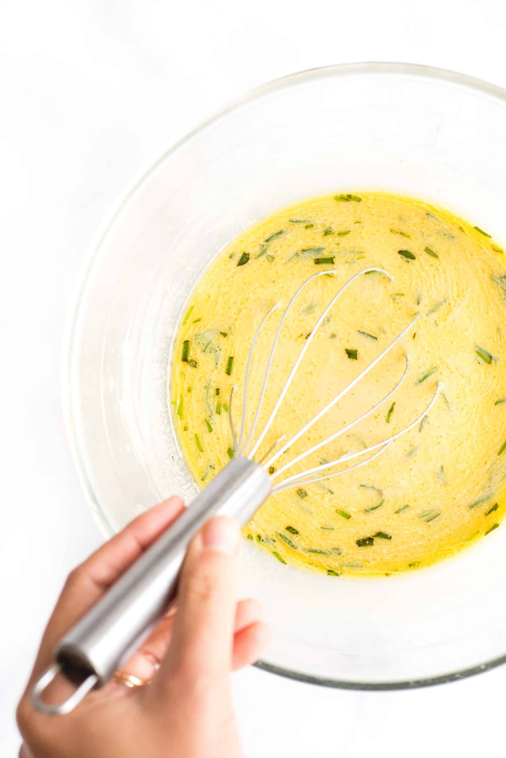 Whisking a yellow mixture in a glass bowl.