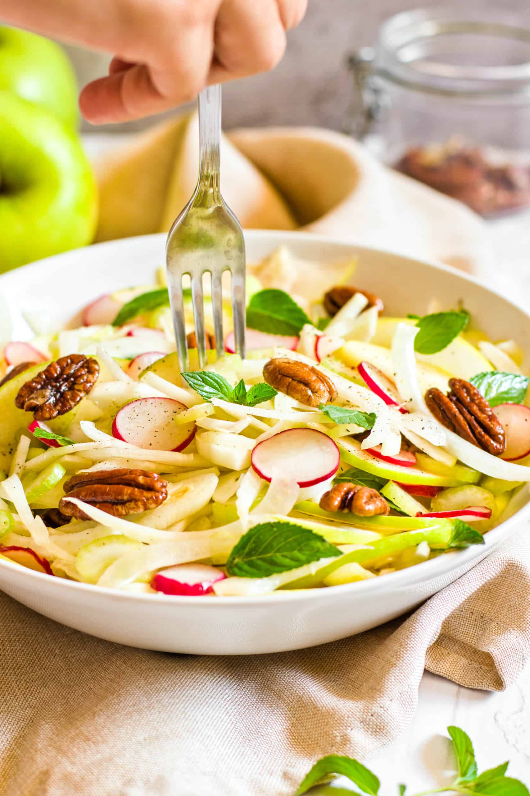 Fork reaching into a bowl of fennel and apple salad.