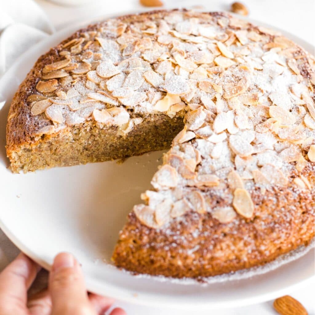 A hand holding a plate of half-eaten cake