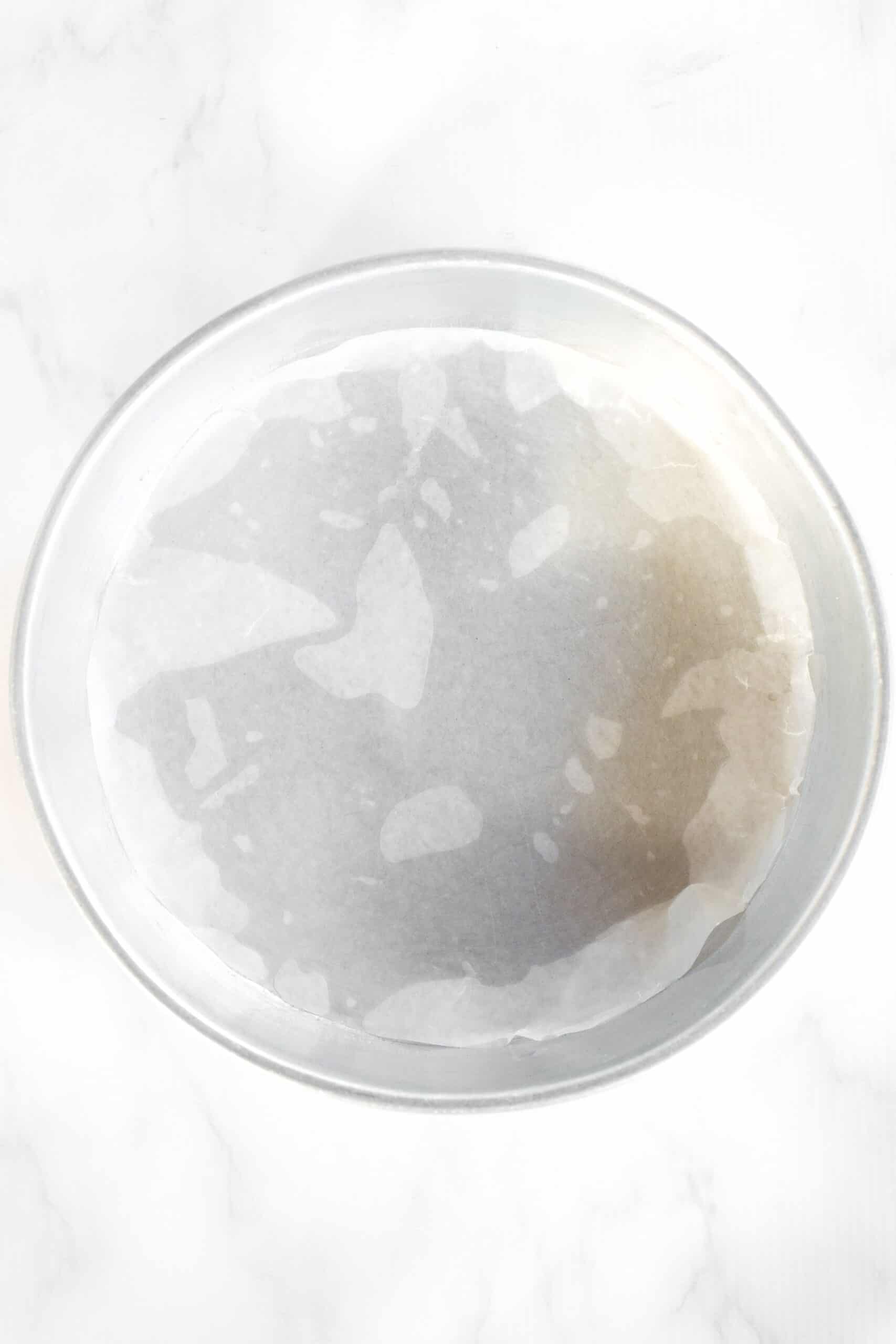 A round metal cake pan lined with parchment paper.