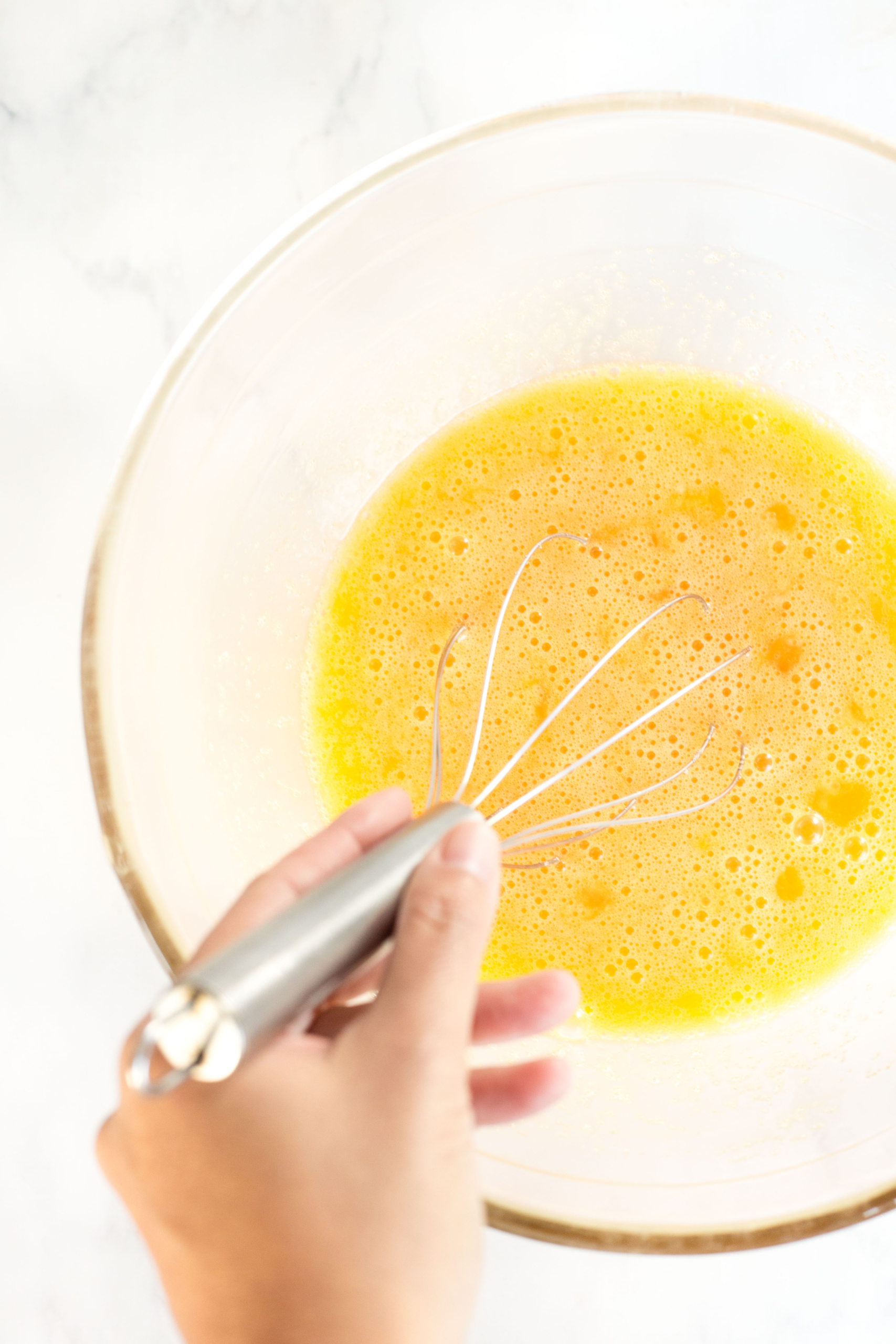 Whisking yellow egg mixture in a glass bowl.