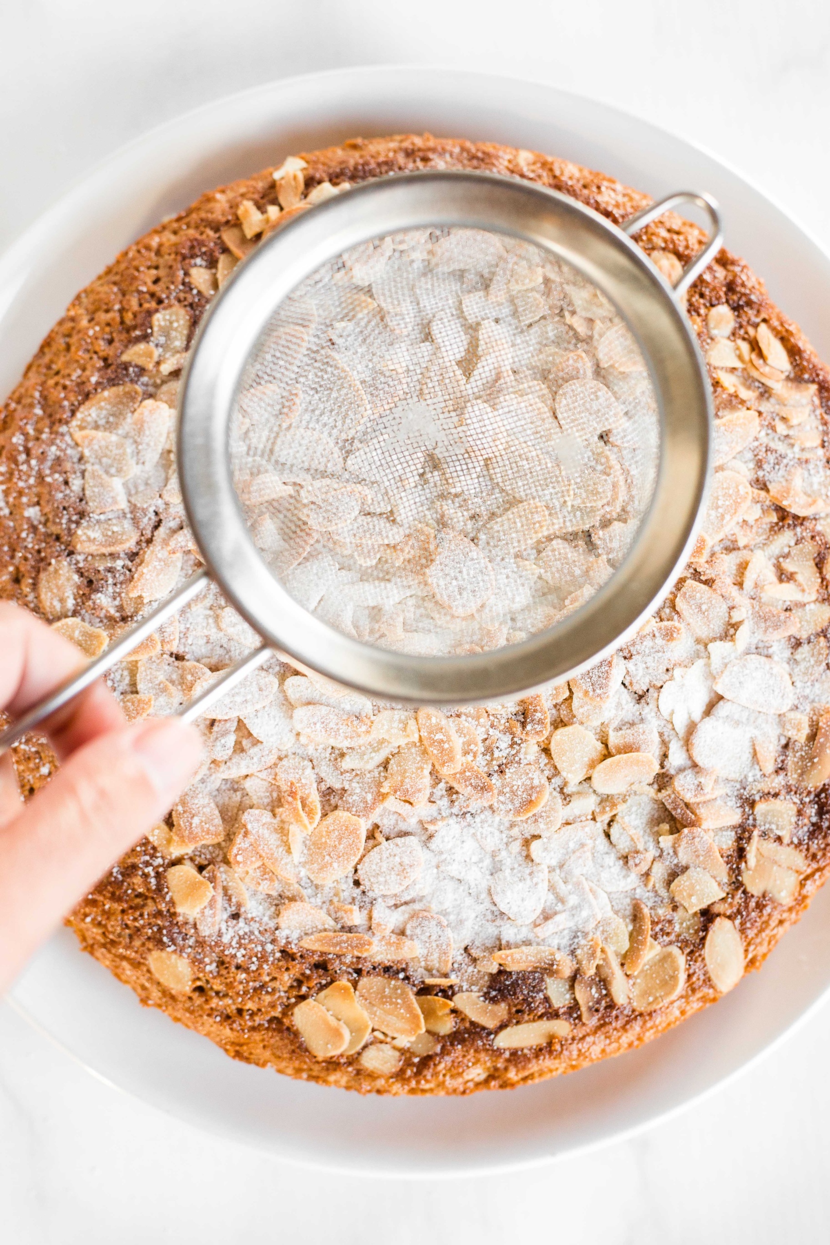 Gluten-Free Almond Cake Recipe (Dairy-Free) Sprinkling powdered sugar on a gluten-free almond cake.