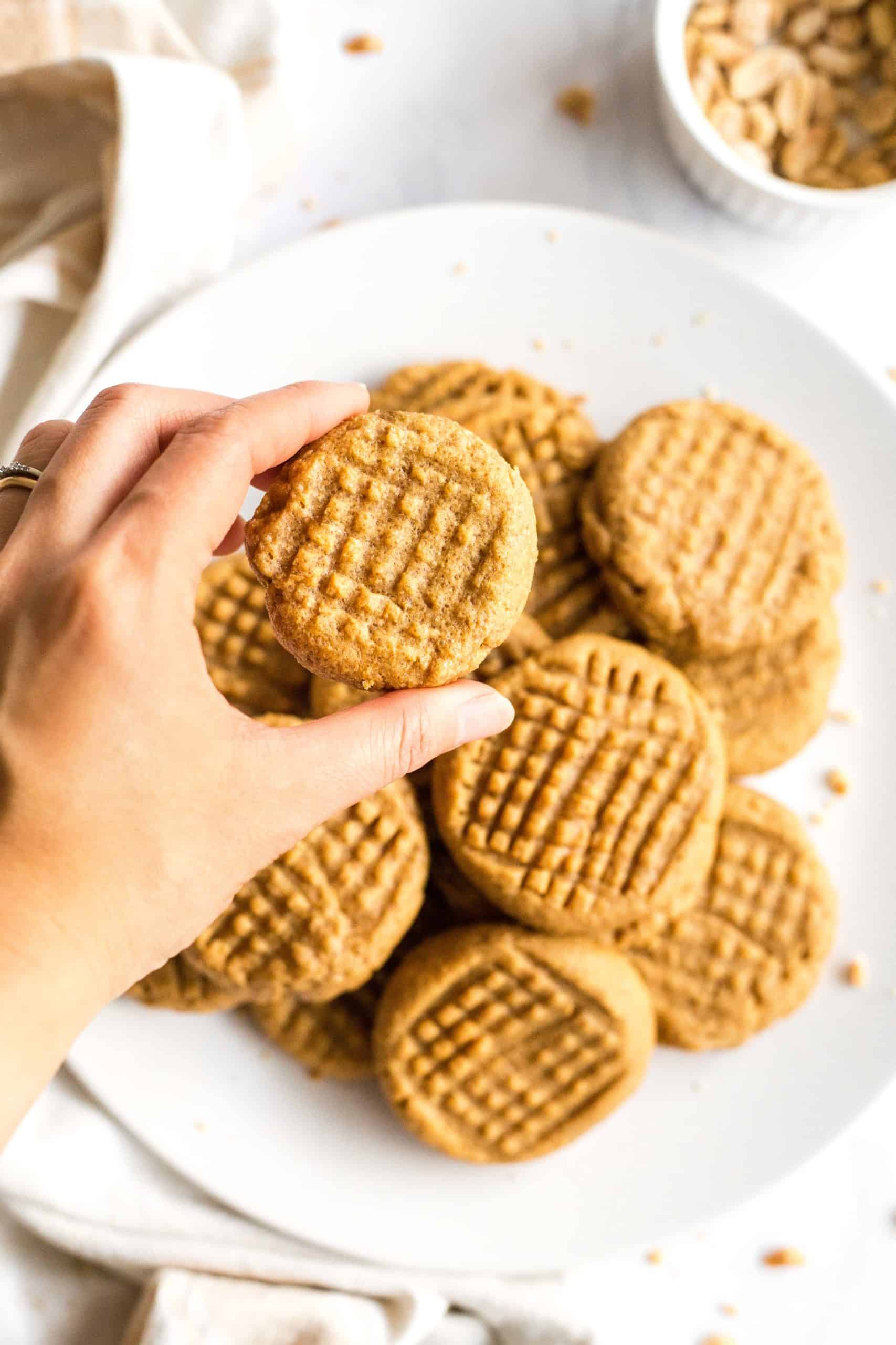 Hand holding up a cookie from a plate of gluten-free peanut butter cookies.