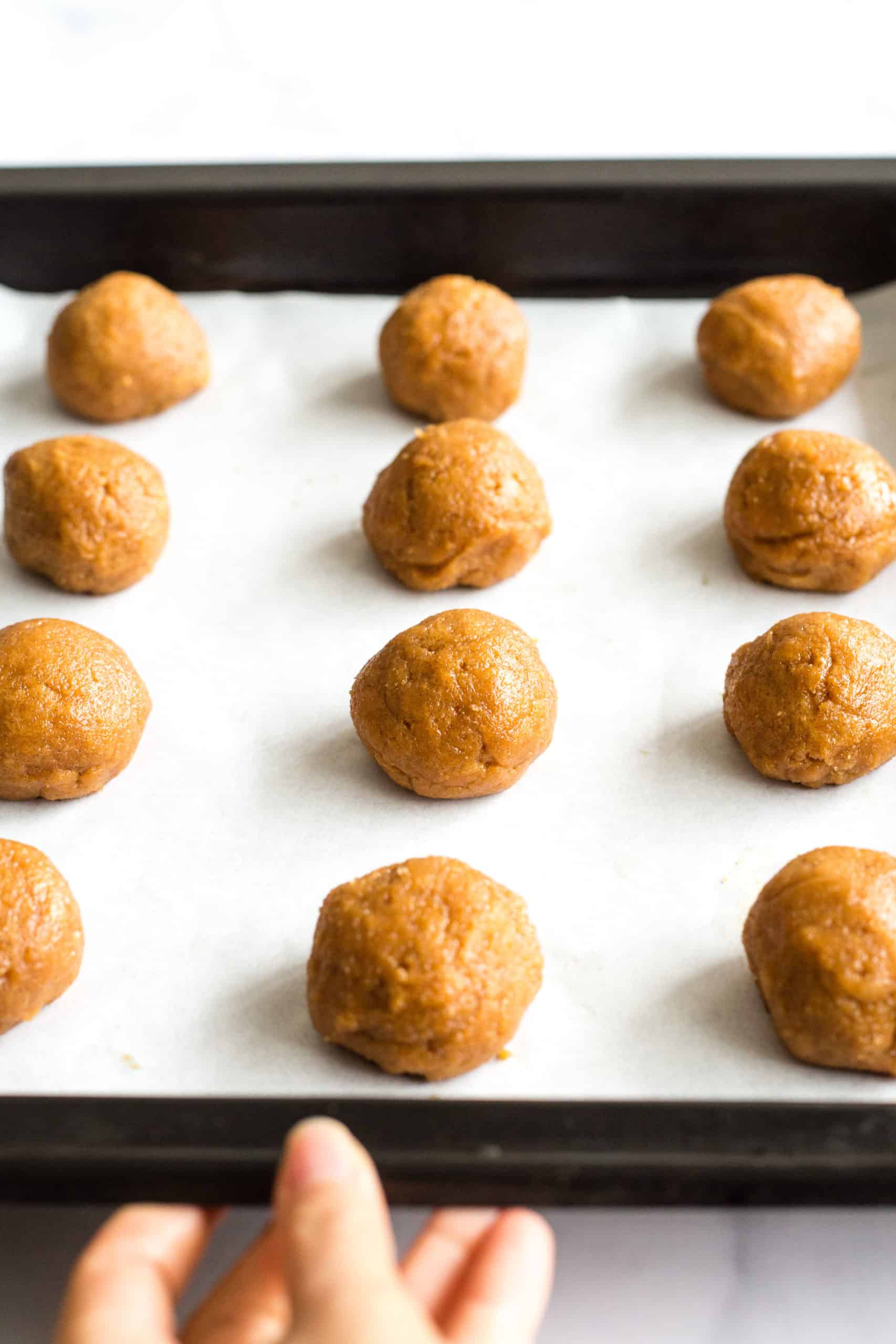 Peanut butter cookie dough balls lined up on a parchment-lined baking sheet.