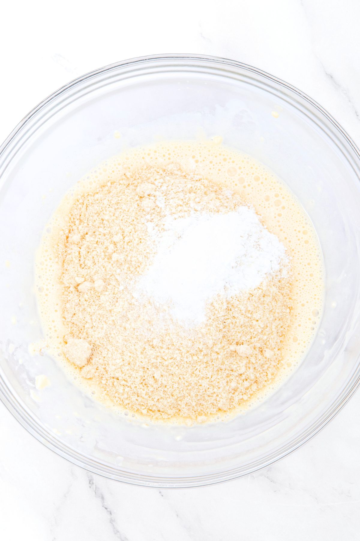 Almond flour and baking powder on top of a bowl of pale yellow liquid
