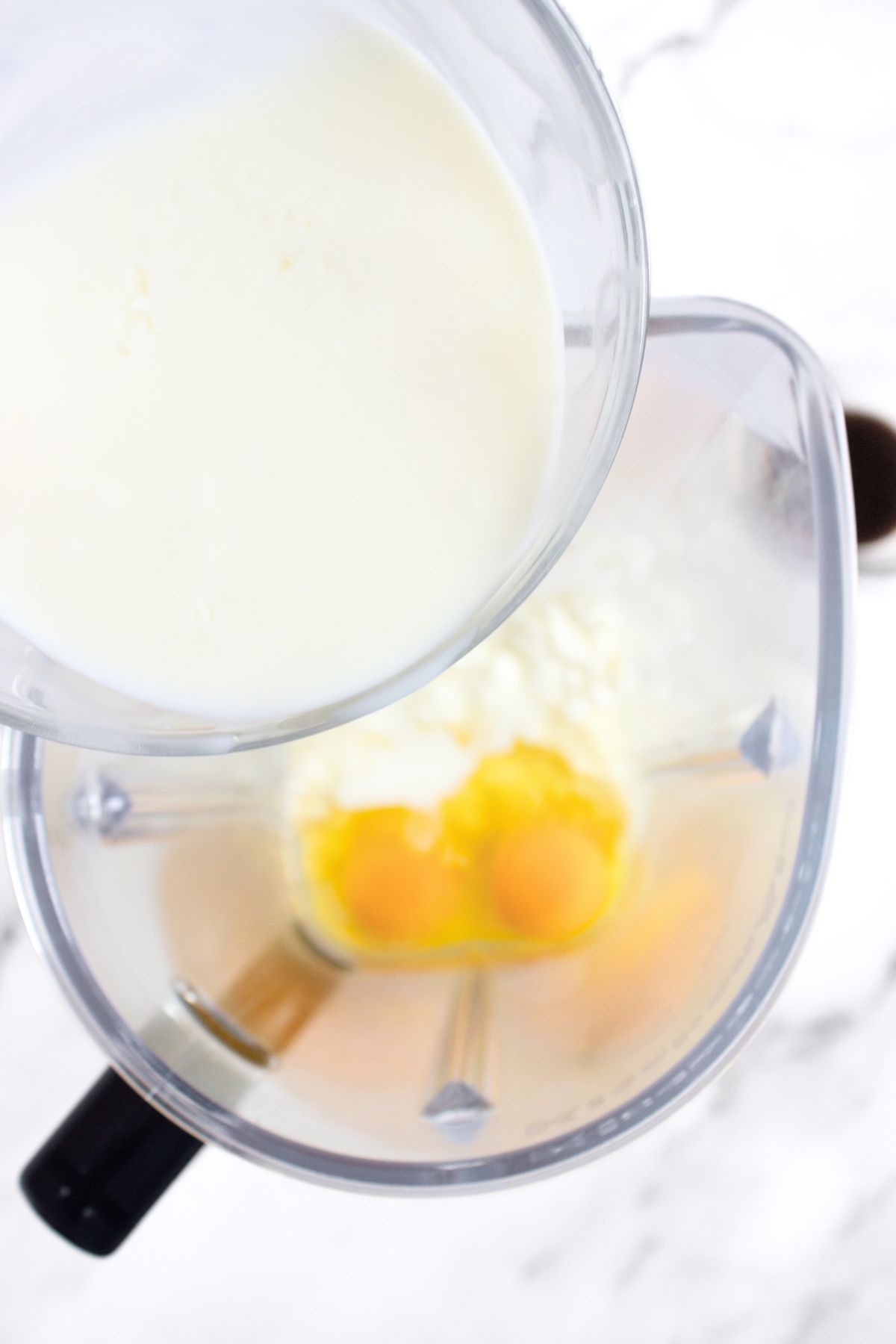Pouring milk into blender bowl with eggs and cottage cheese.