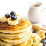 A stack of fluffy gluten-free pancakes topped with blueberries and bananas.