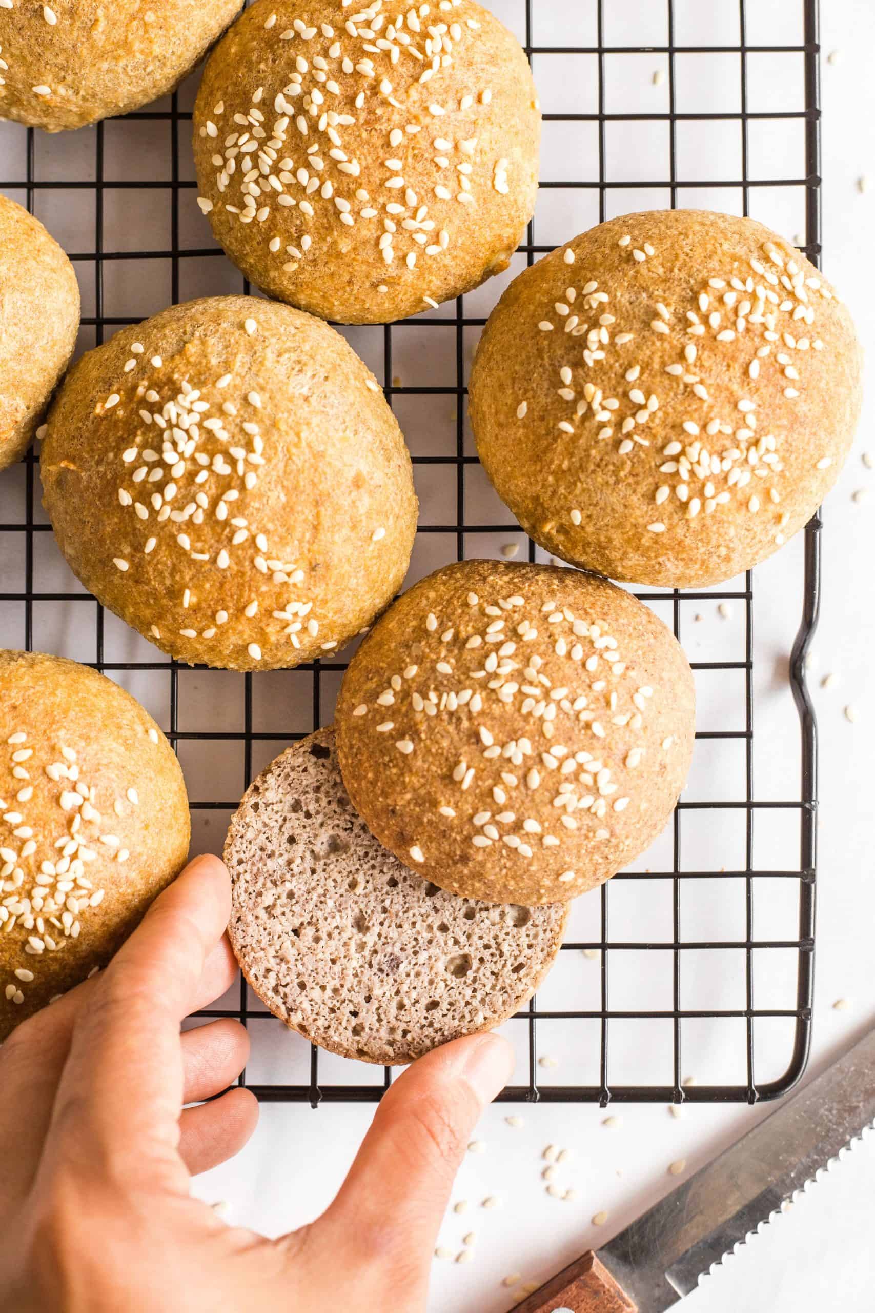 Hand reaching for a sliced low carb bun along with others on a wire rack.