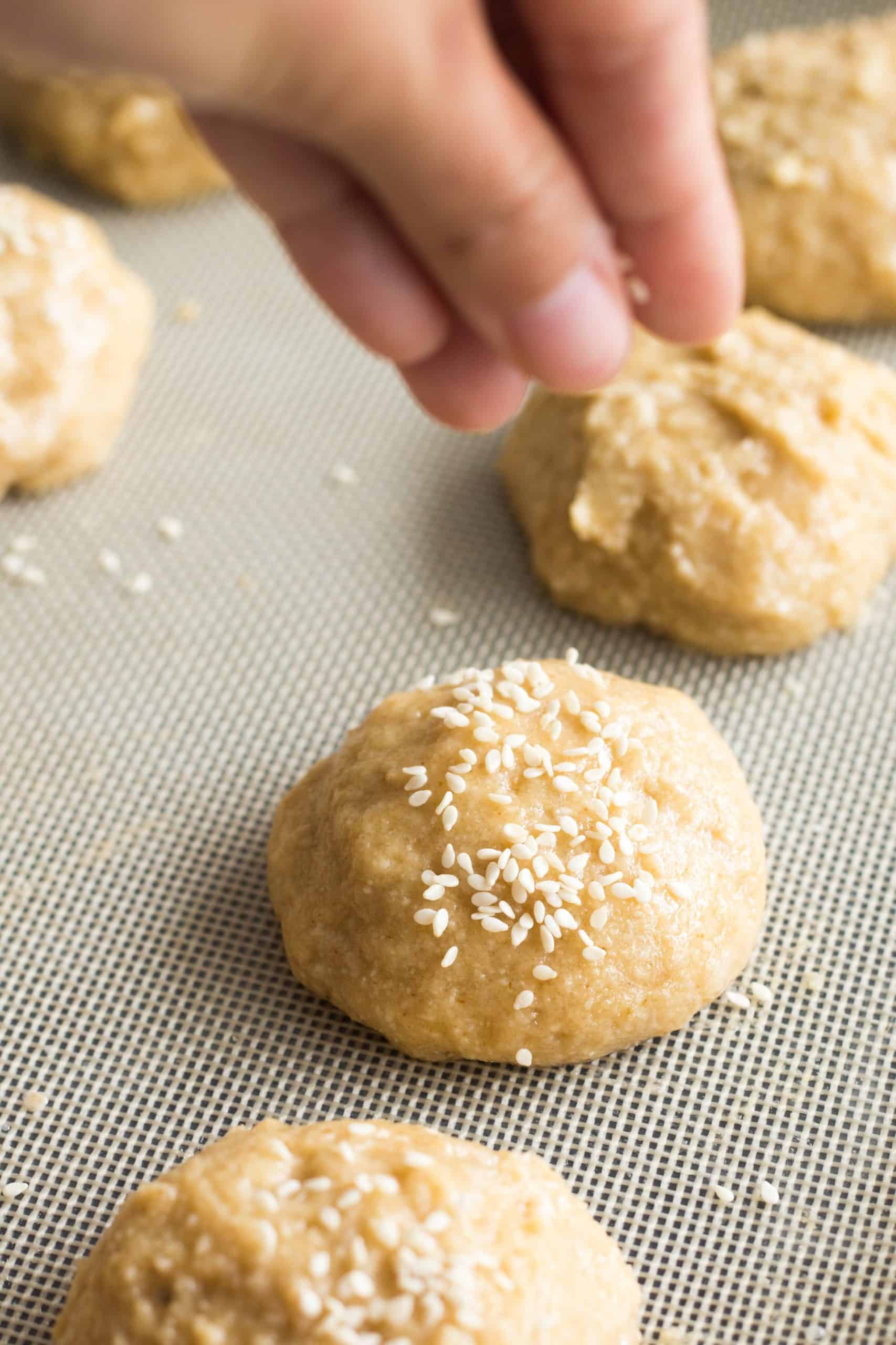 Sprinkling sesame seeds on top of dough balls.