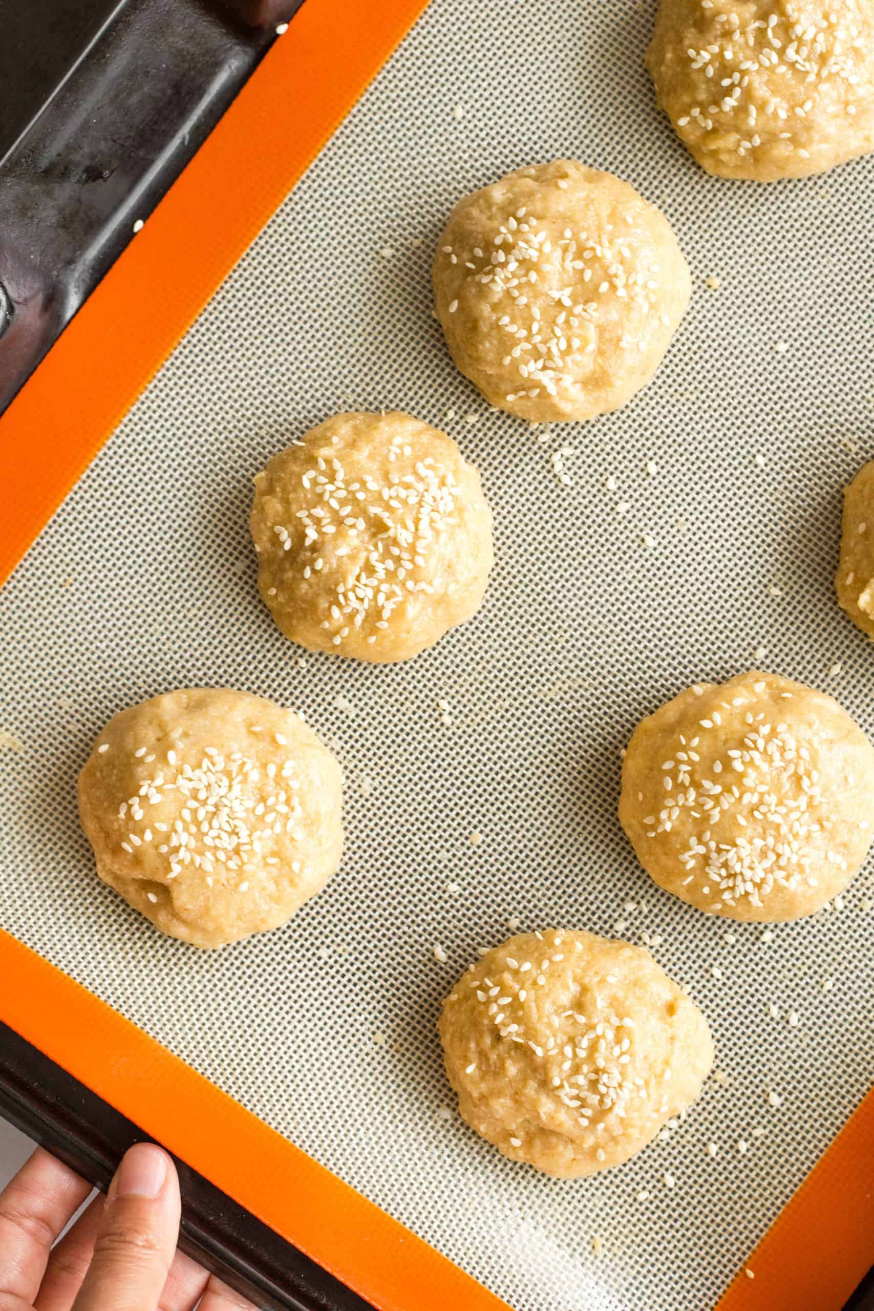 Raw dough balls on a silpat-lined baking sheet.