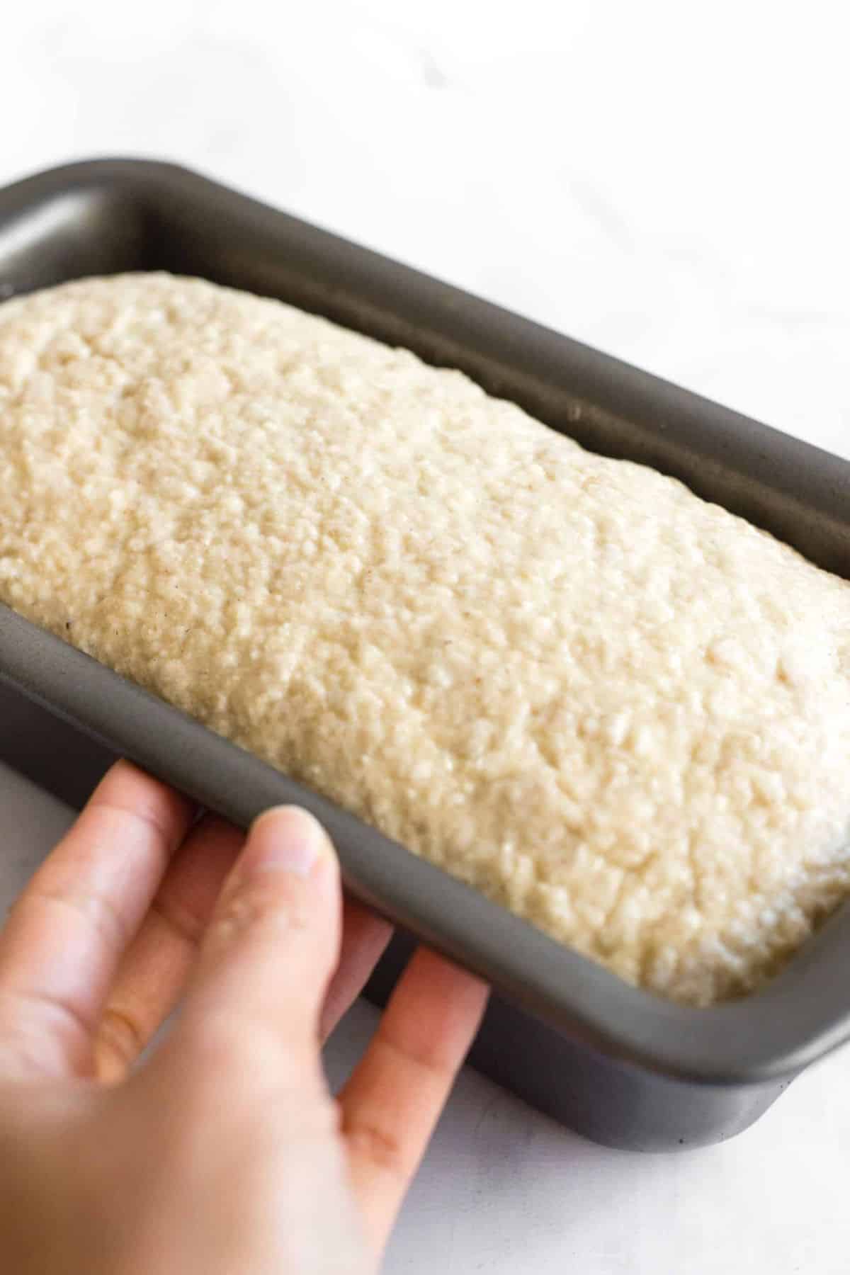 Holding a pan with risen bread dough.