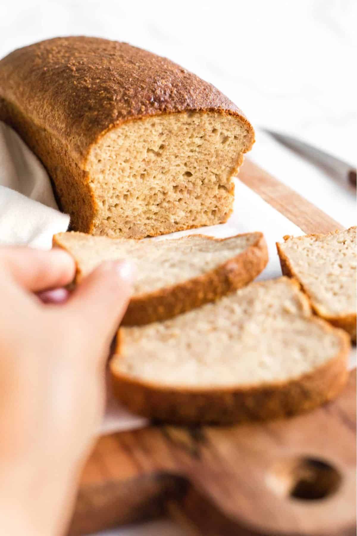 Reaching for a slice of gf quinoa flour bread from parchment-lined board.