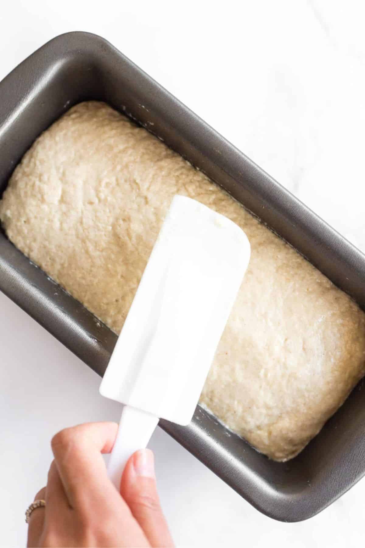 Smoothing out bread dough in metal loaf pan.