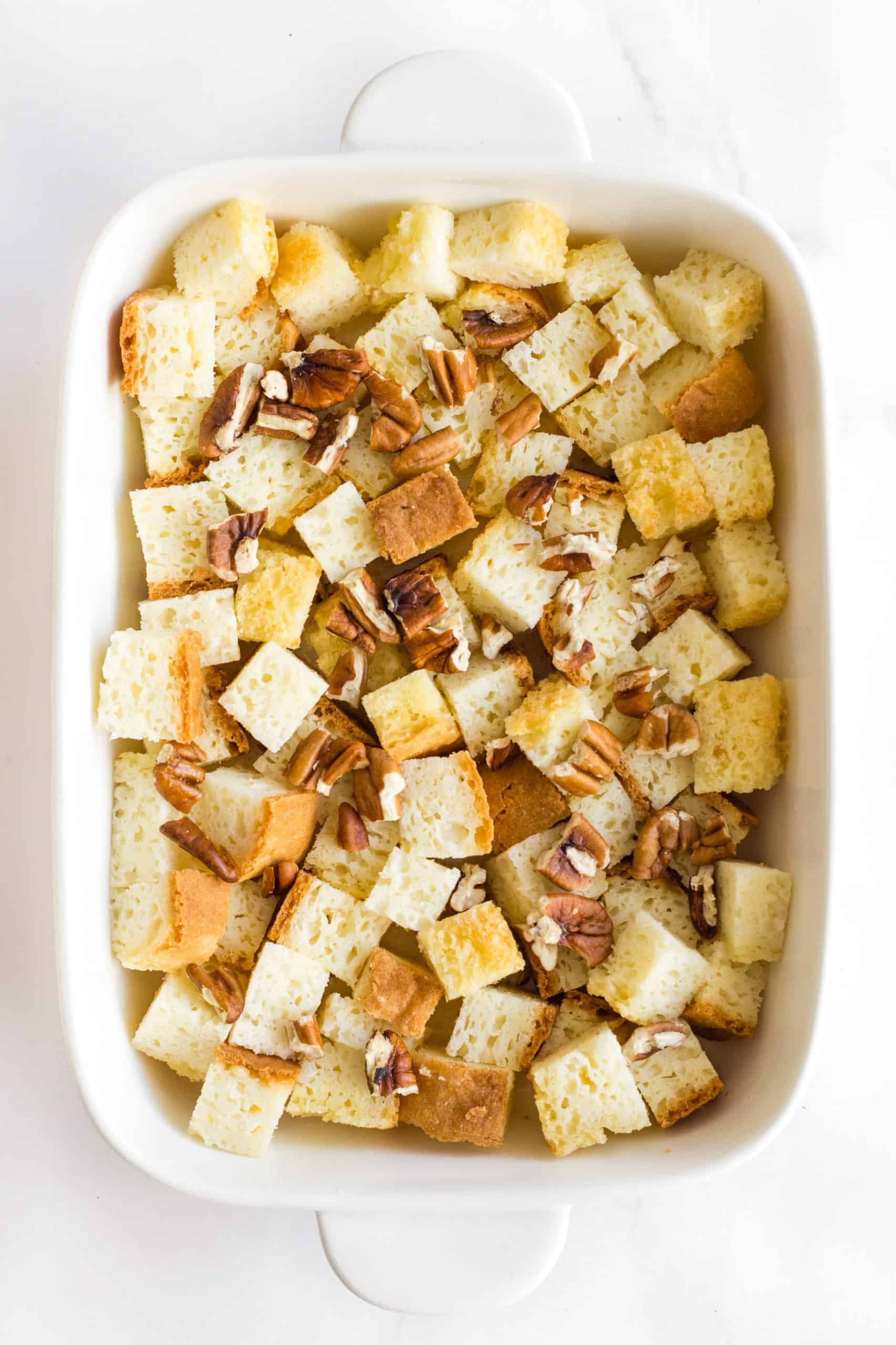 A casserole dish with bread chunks and chopped pecans.