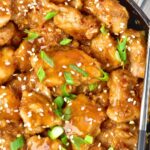 Chopsticks on top of a skillet of chicken topped with green onions