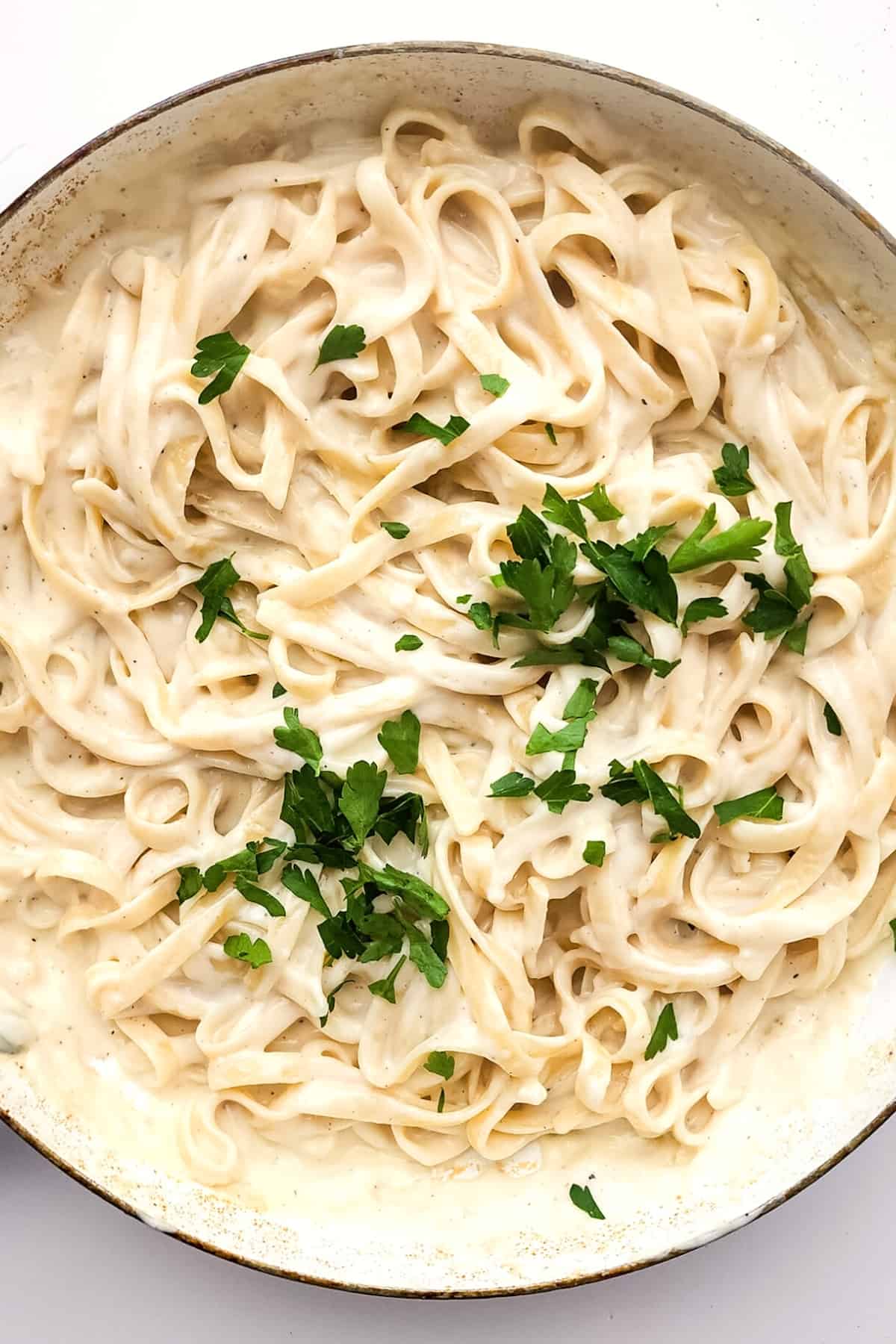A big pan with fettuccine alfredo sprinkled with fresh parsley.