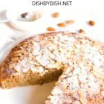 A half-sliced flourless almond cake on white plate.