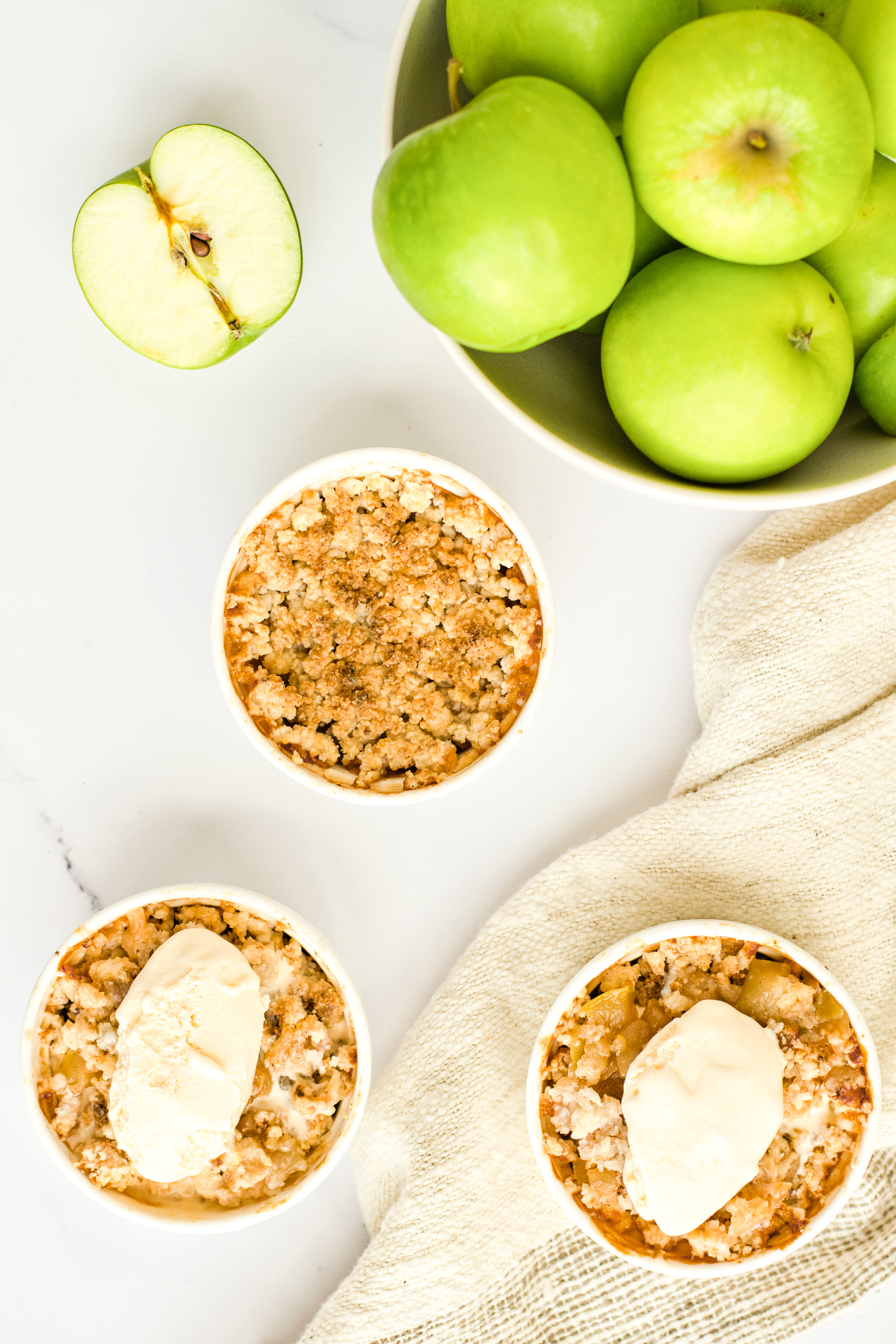 Vegan apple crumble in ramekins on a marble board next to a bowl of green apples.