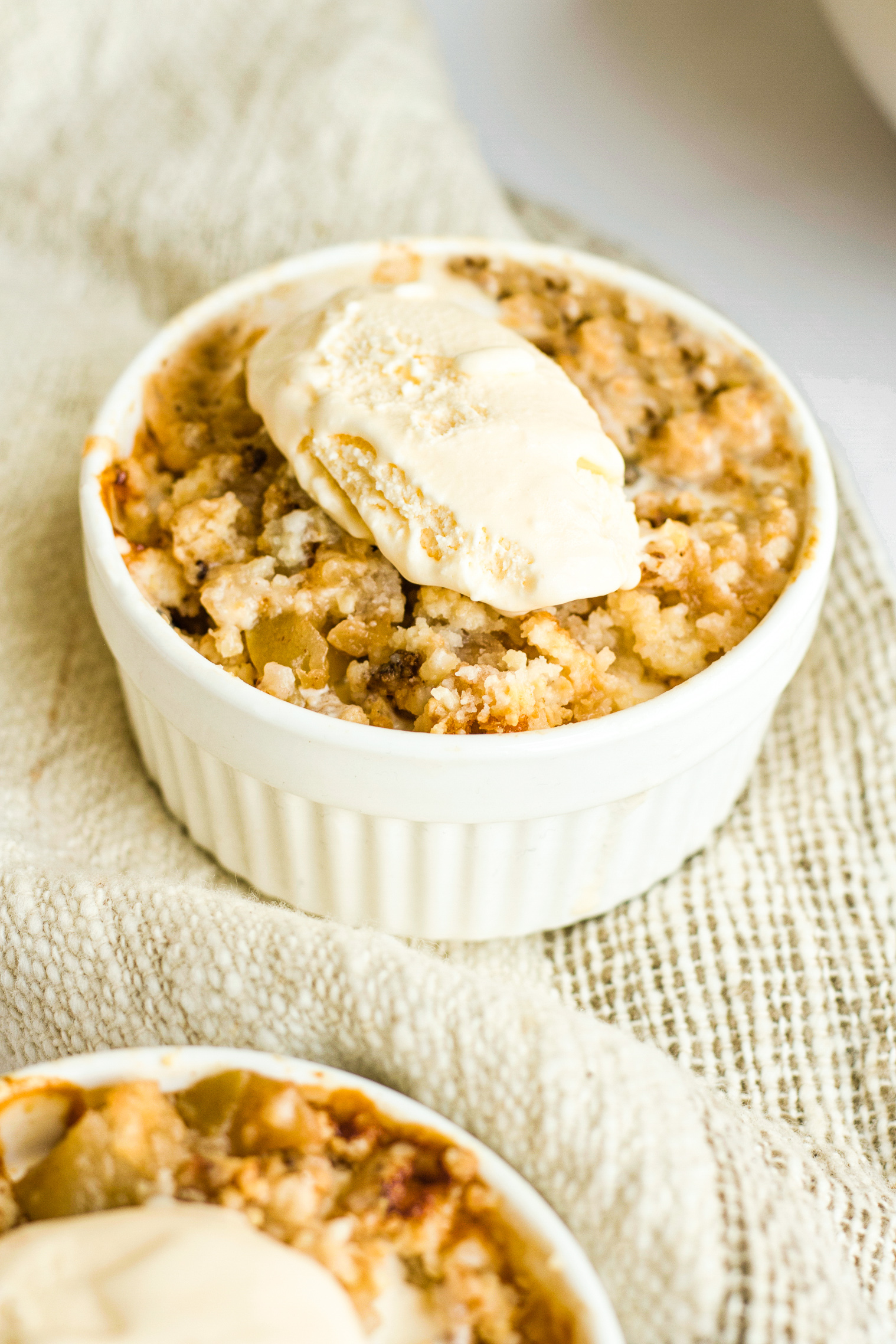 A ramekin with ice cream topped gluten-free apple crumble.