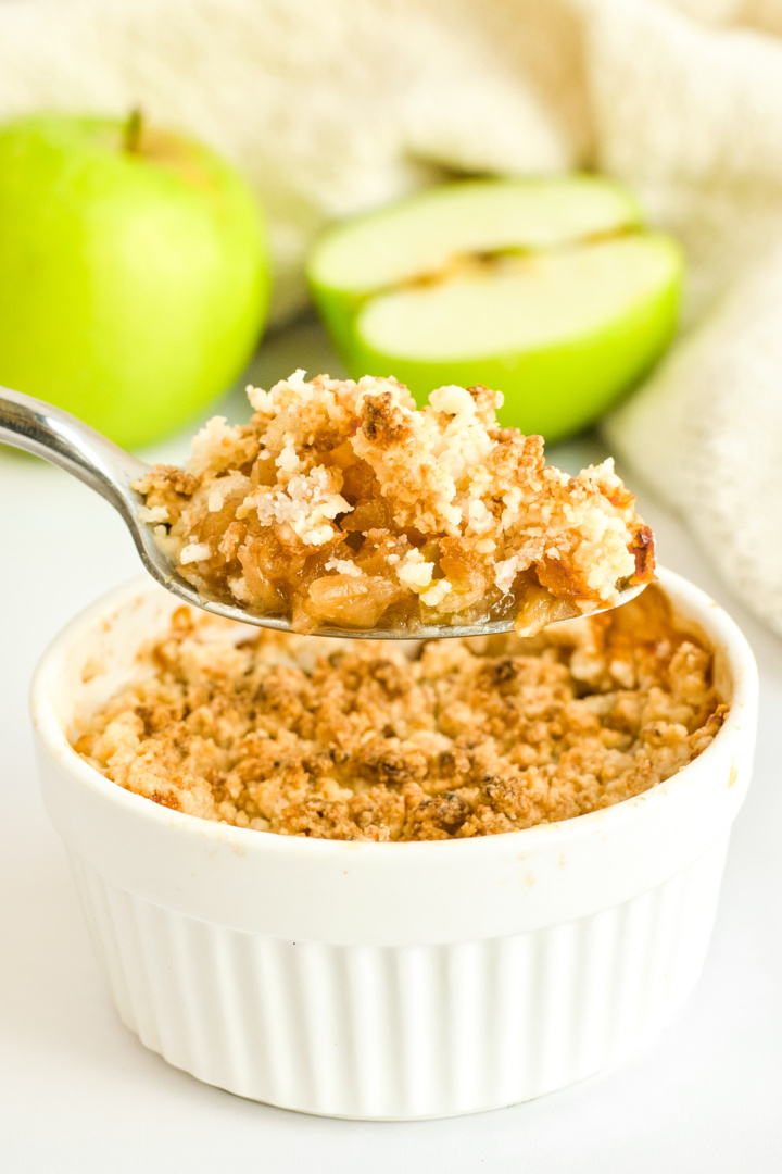 Holding up a spoonful of apple crumble from ramekin