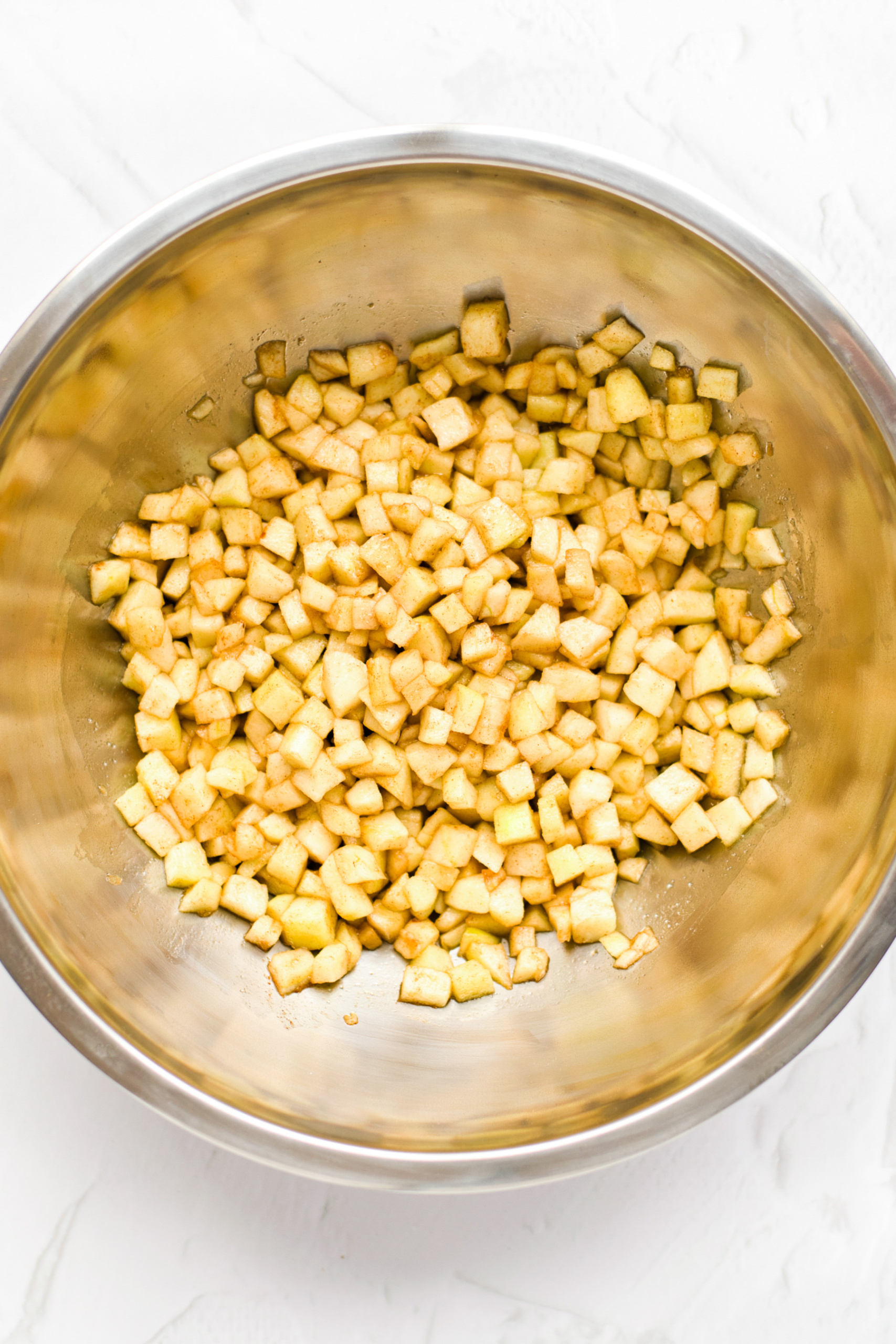 Cubed apples tossed with cinnamon and sugar in a metal bowl.