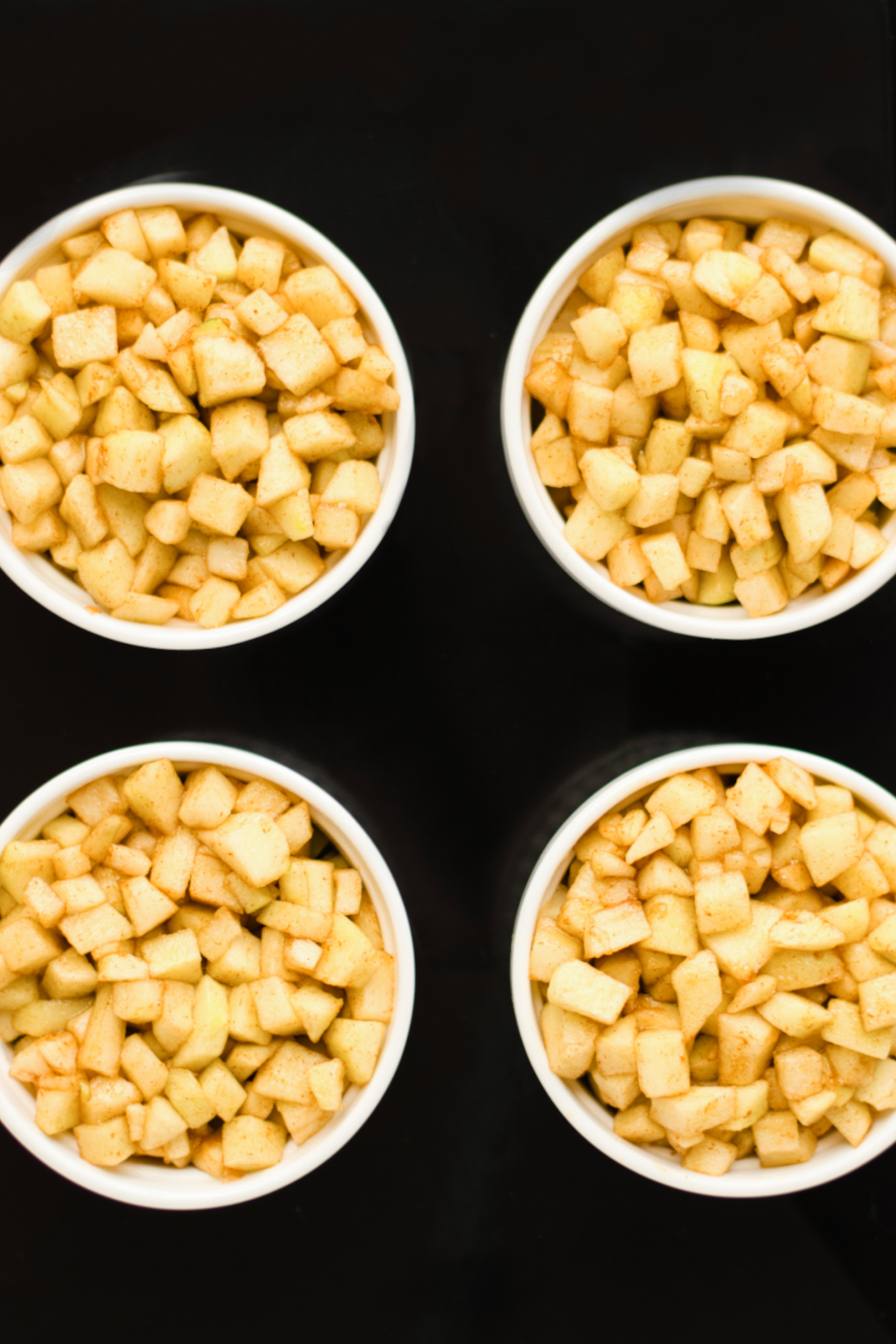 Cinnamon apples in white ramekins on baking sheet.