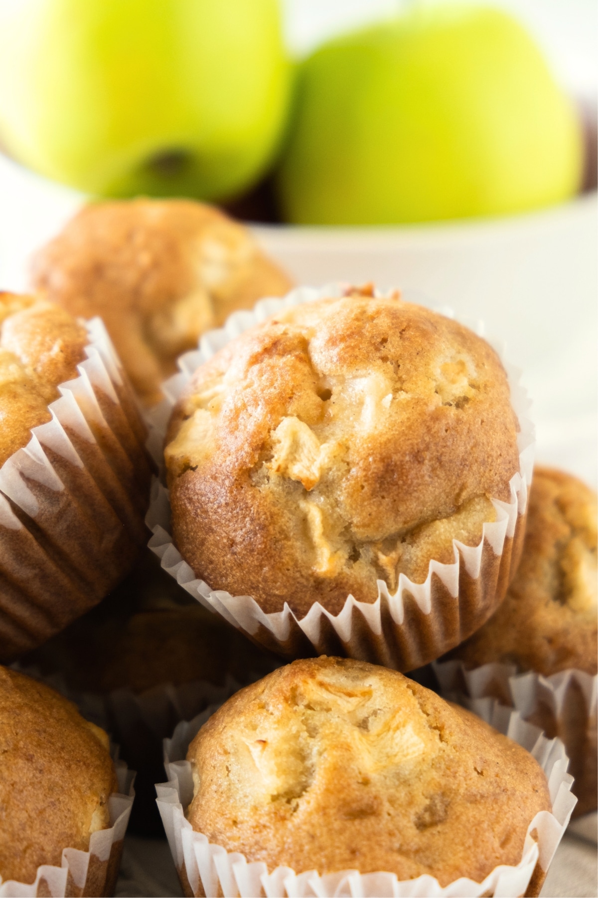 A stack of gluten-free apple muffins in front of green apples.