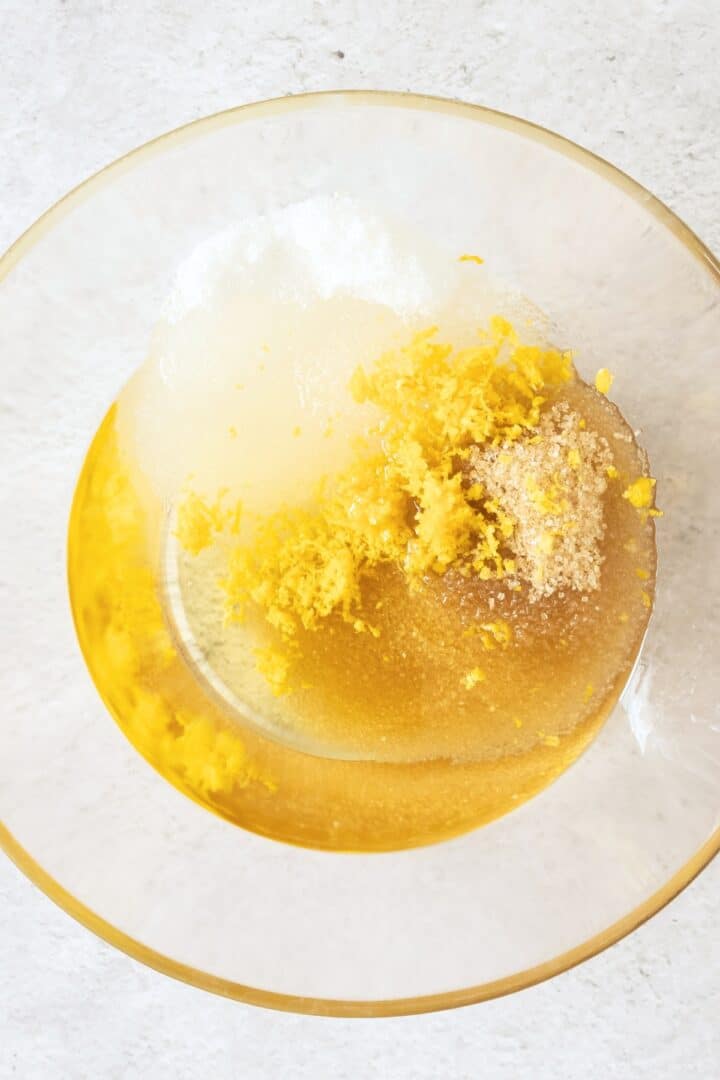 Grated lemon zest, sugar, oil in glass mixing bowl.