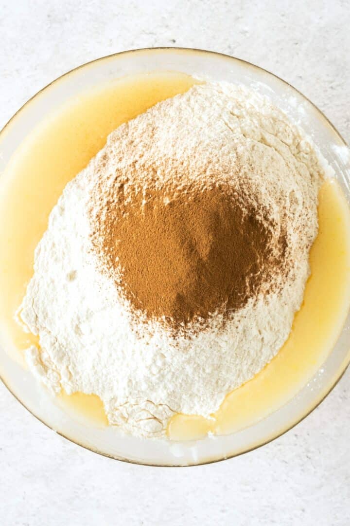 Flour mixture and ground cinnamon on top of pale yellow batter.