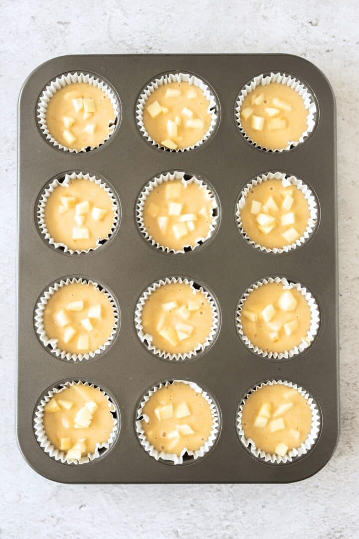 Cubed apples and muffin batter in muffin pan.